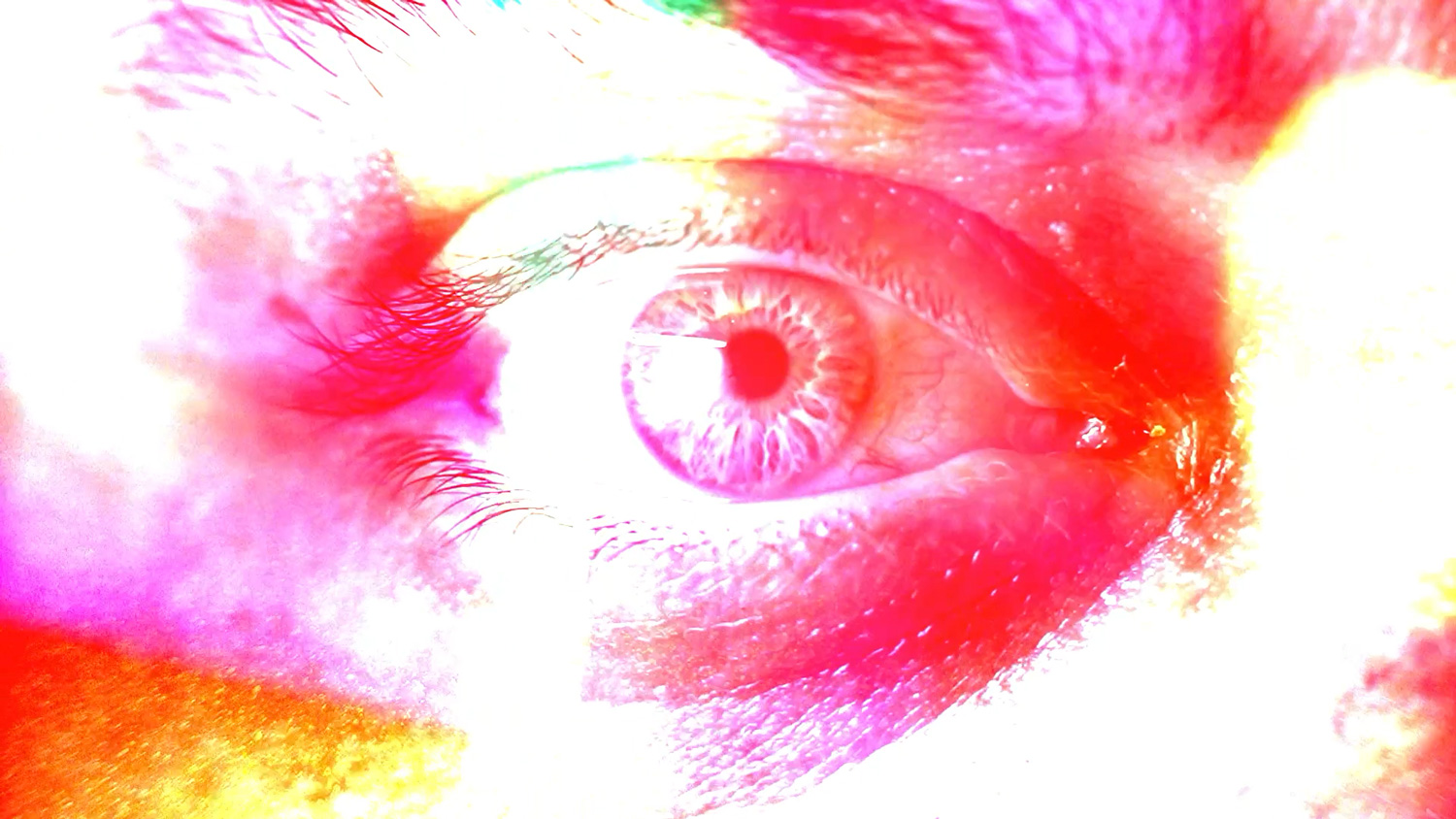 Extreme close-up of a human eye saturated in clashing red, pink and orange tones, from the Overstimulated video piece