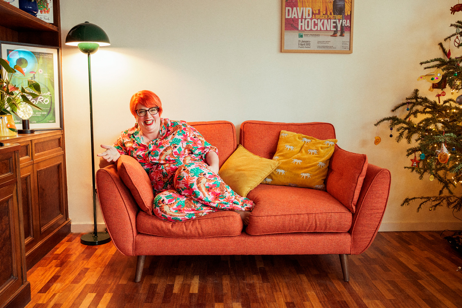 A woman sitting on a couch with bright orange hair and a big smile